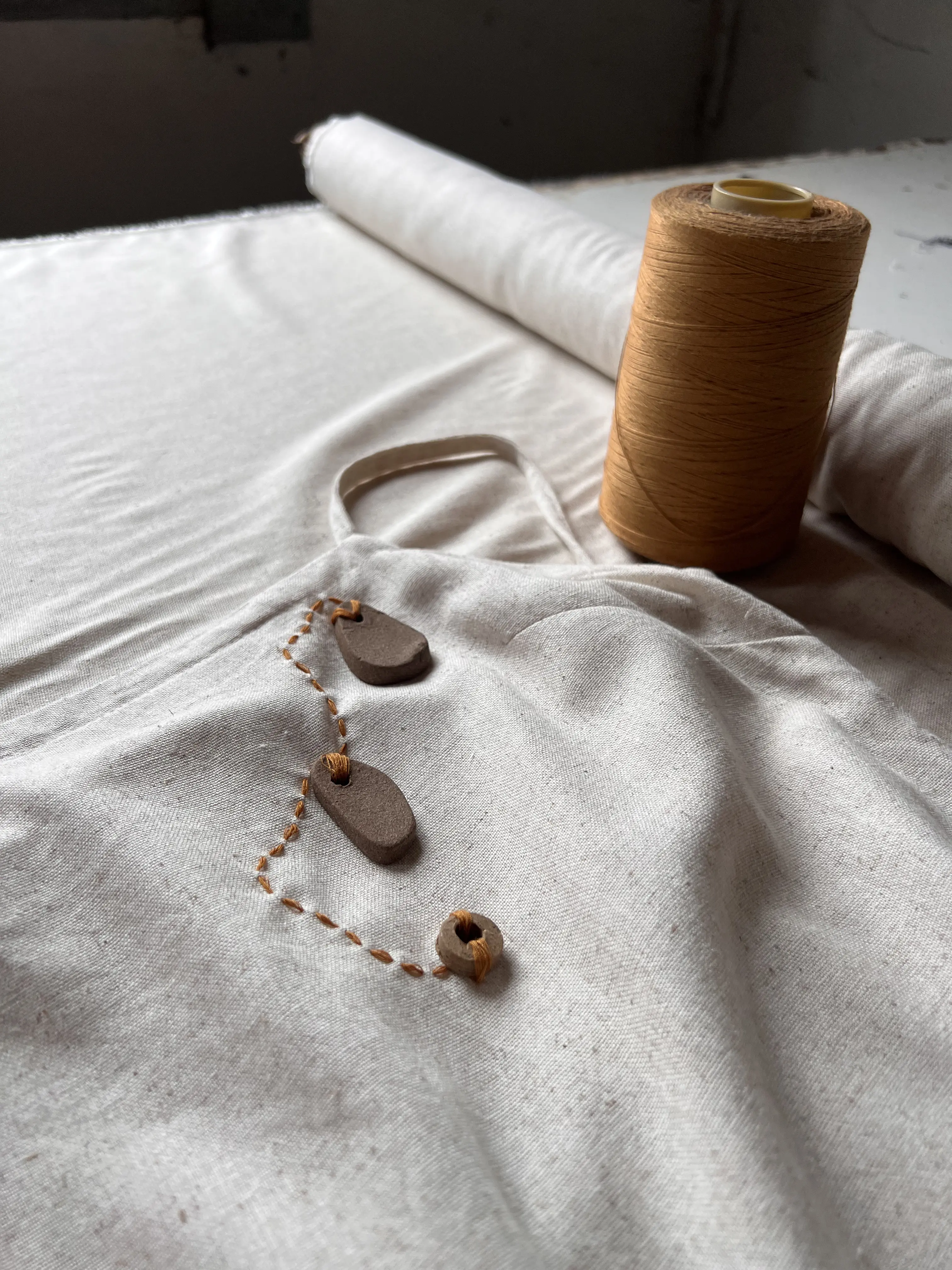 Tecido branco com botões artesanais e carretel de linha mostarda, representando o artesanato da marca Sivirina